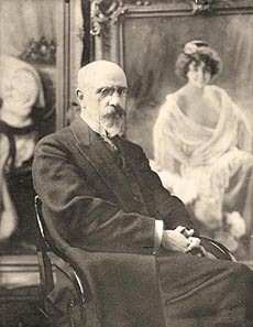 Victor Stember in later life, seated in his studio in front of his portraits of women