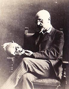 Victor Stember seated in an armchair holding a skull, an artist’s anatomy study prop